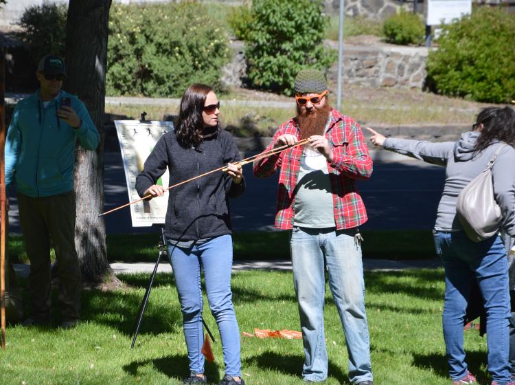 Bend Oregon Archaeology Roadshow volunteer explains how to use the atlatl spear thrower to a visitor at the 2019 event; photo by Beverly Clement