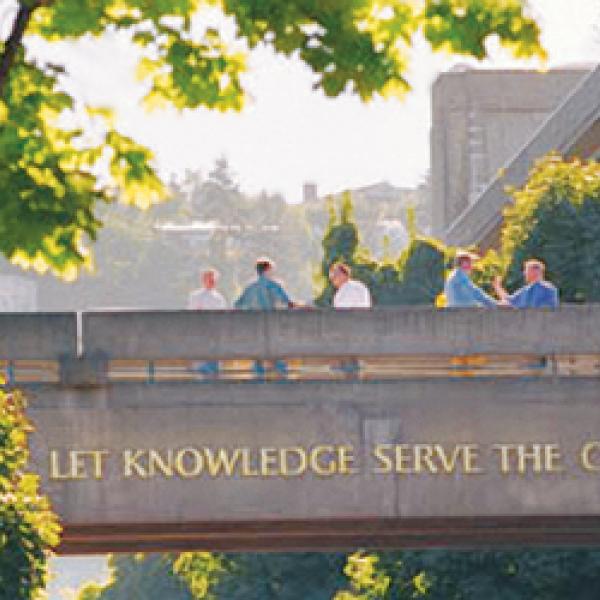 Photograph of skybridge with PSU's motto: "Let Knowledge Serve The City". Five people are standing on the skybridge, talking to each other.