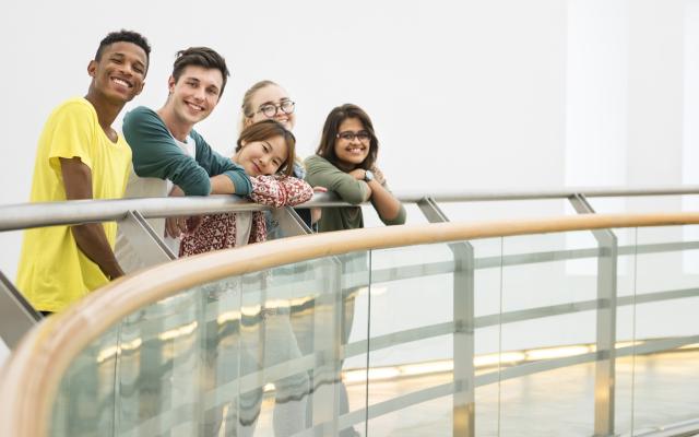 A diverse group of students gather around a curved railing, smiling at the viewer.