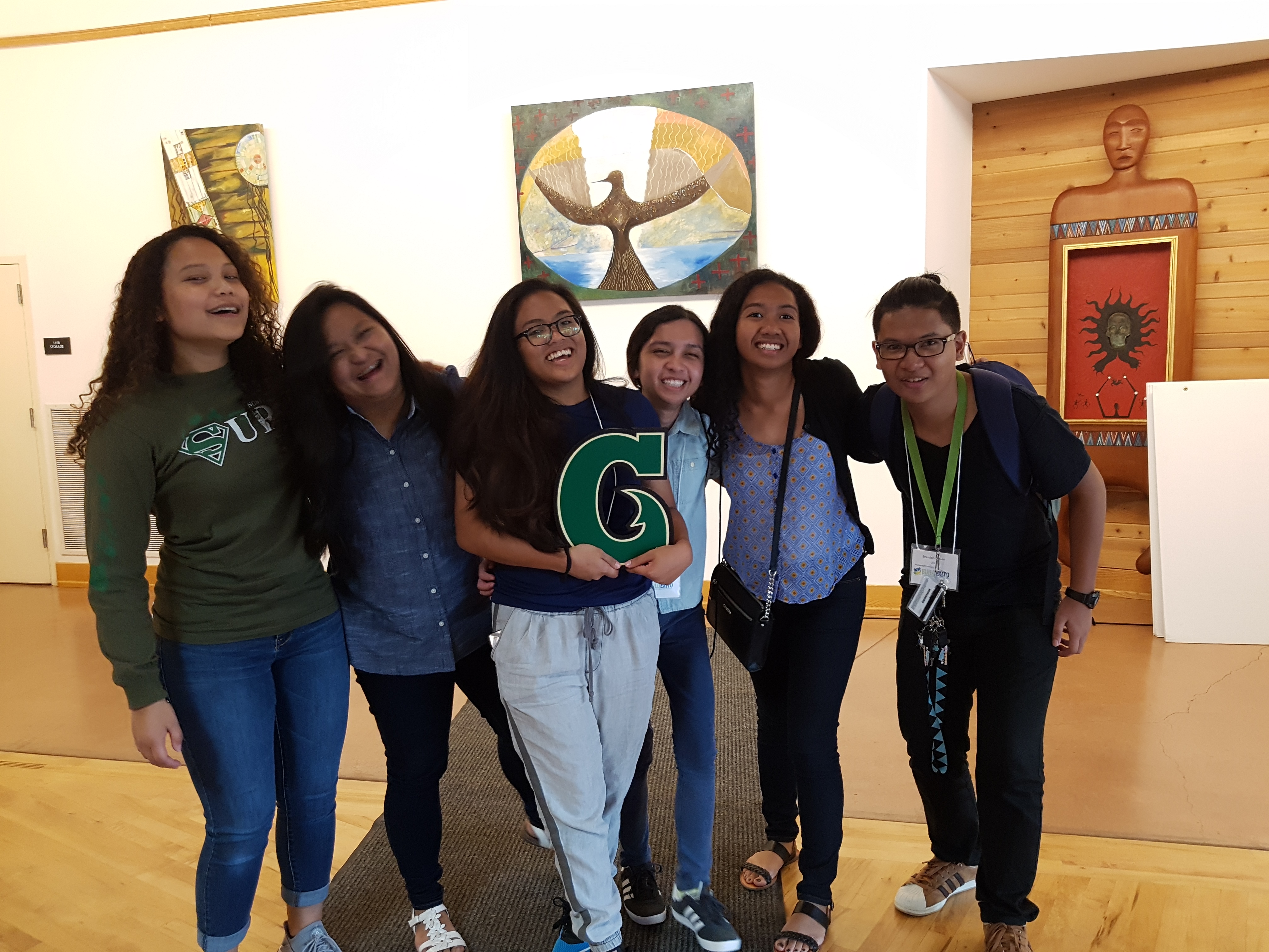A group of students from the University of Guam poses together, holding a printed University of Guam logo in the middle.