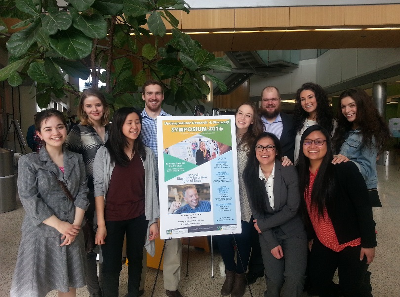 9 students and faculty stand next to a poster