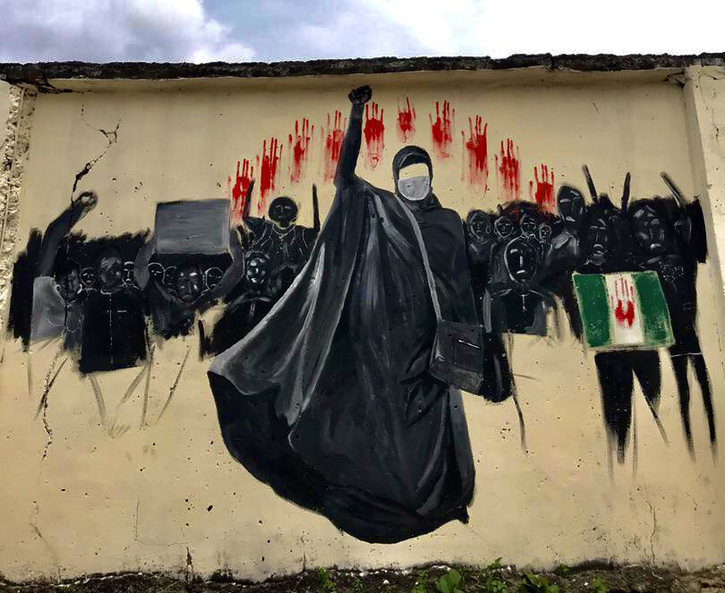 Wall Graffiti of #EndSARS protesters in black clothing with masks and red hand prints featuring the face of the protest, Mrs. Aisha Yesufu