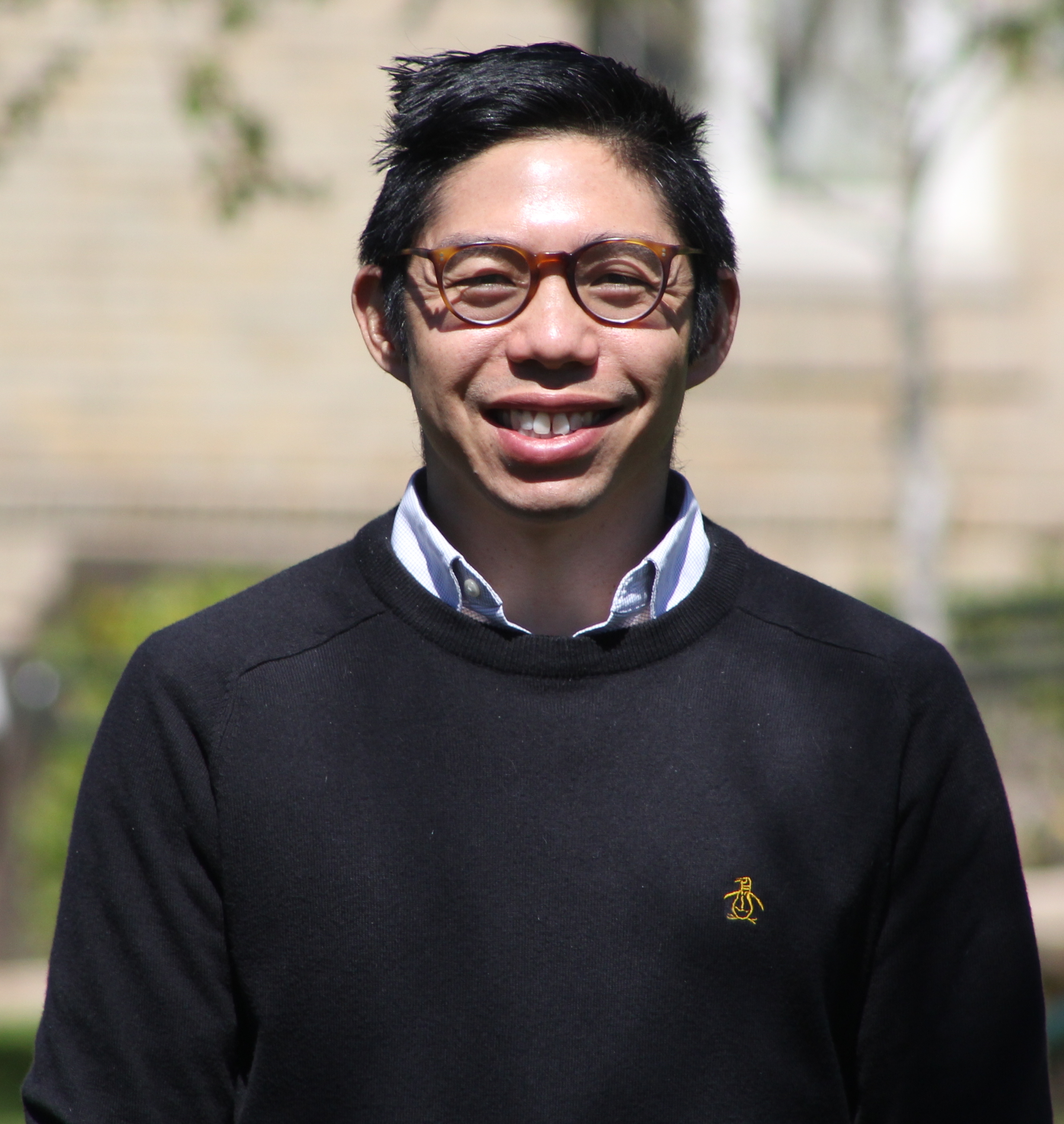 Photo of Brian Chan wearing a black sweater and glasses. 