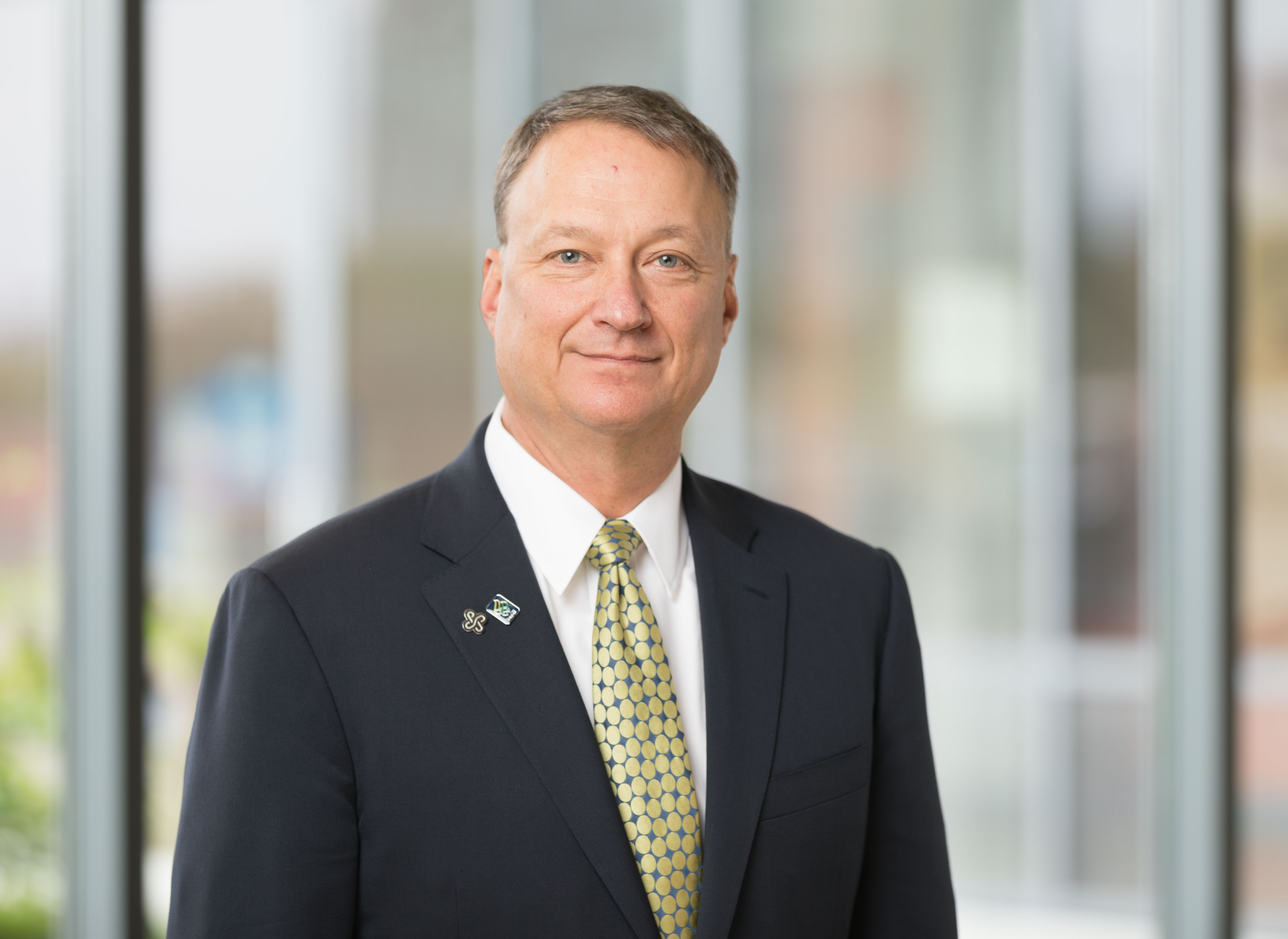Photo of David Bangsberg, MD, MPH, wearing a suit and green and blue tie.
