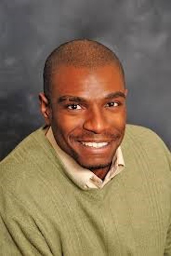 Photo of Seth Pickens wearing a green sweater. He is in front of a gray background.