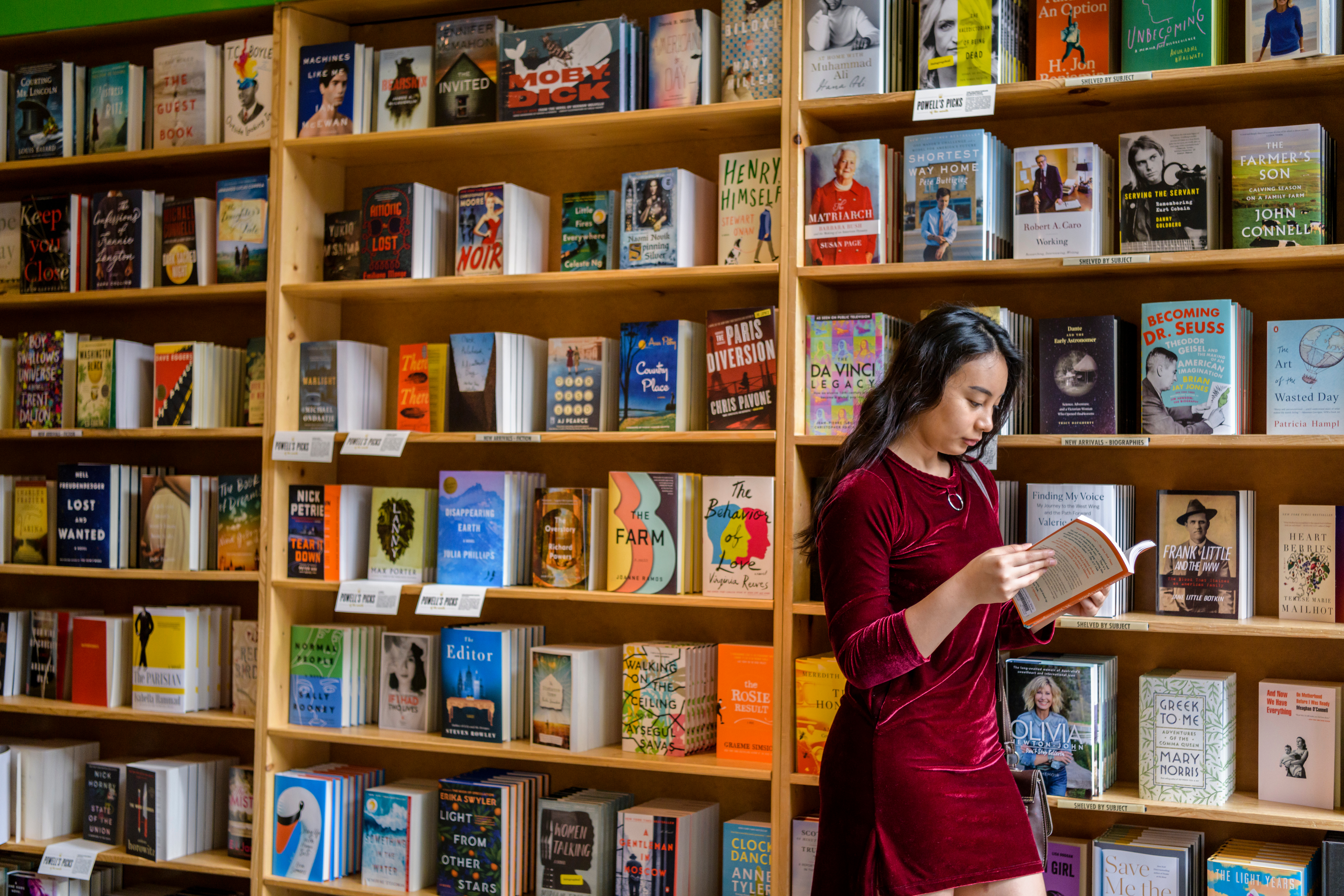 Student standing in front of bookshelves in a bookstore reading a book.