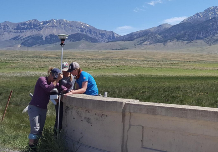 Three students taking measurements with mountains in background