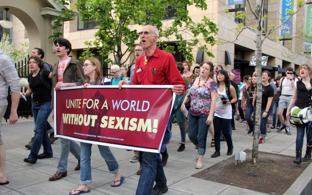 Group of people marching with sign that reads, "Unite for a World Without Sexism"