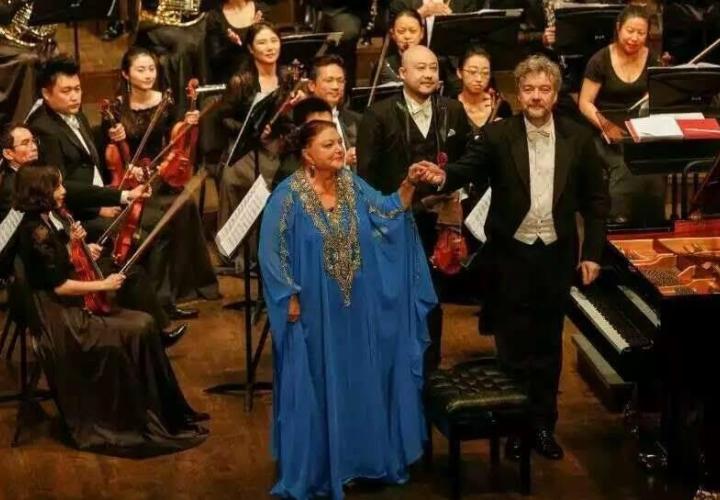 Pianist Oxana Yablonskaya holding the hand of an orchestra conductor with the orchestra in the background.