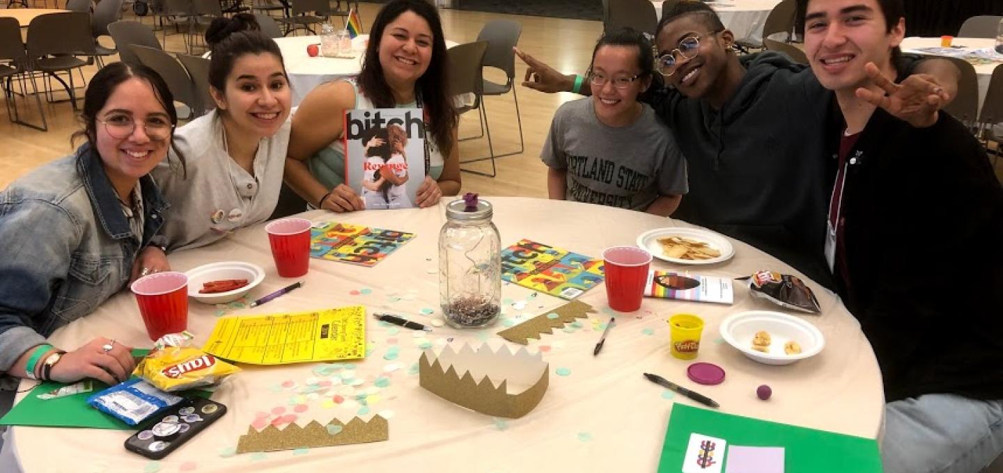 a group of QTBIPOC do crafts around a table with one another and smile with arms around each other