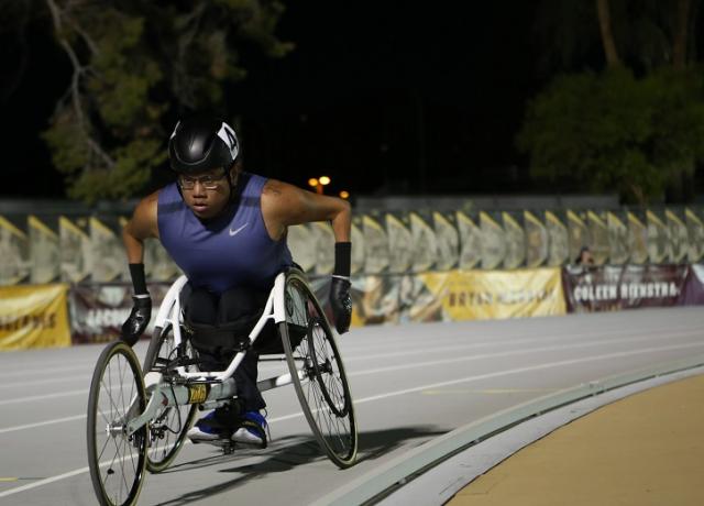 The image is of a person in a wheelchair exercising on an outdoor track. 