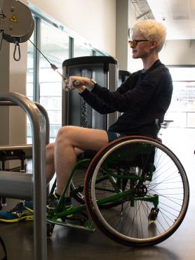 Wheelchair user performing a strength exercise on a machine in the Weight Room.