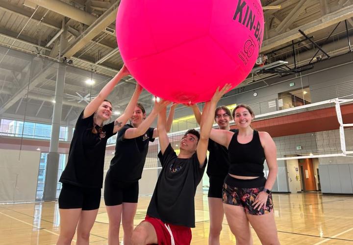 5 people all holding up a giant pink volleyball