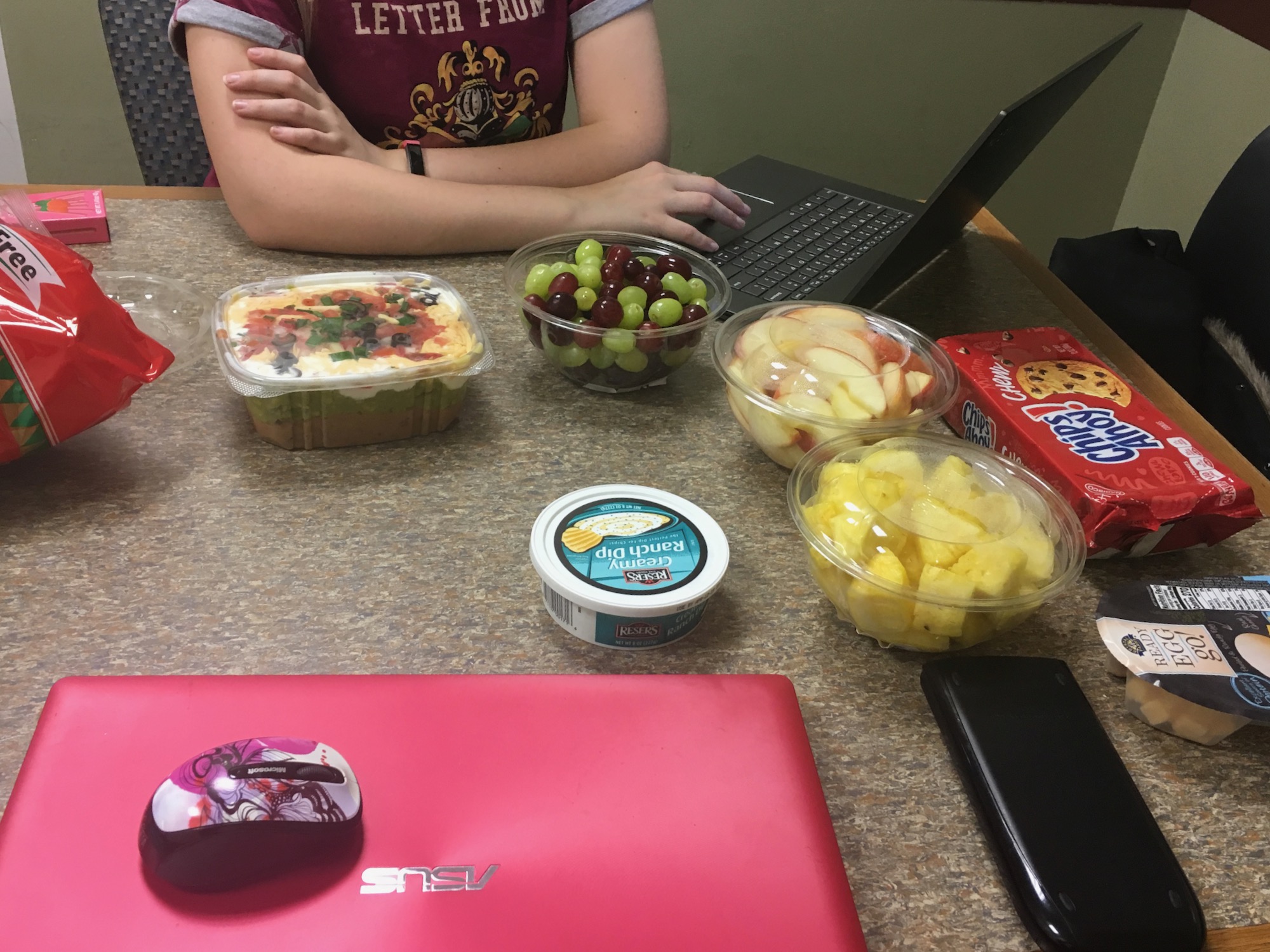 There is a person working on a laptop, there are several snacks on the table around the laptop.