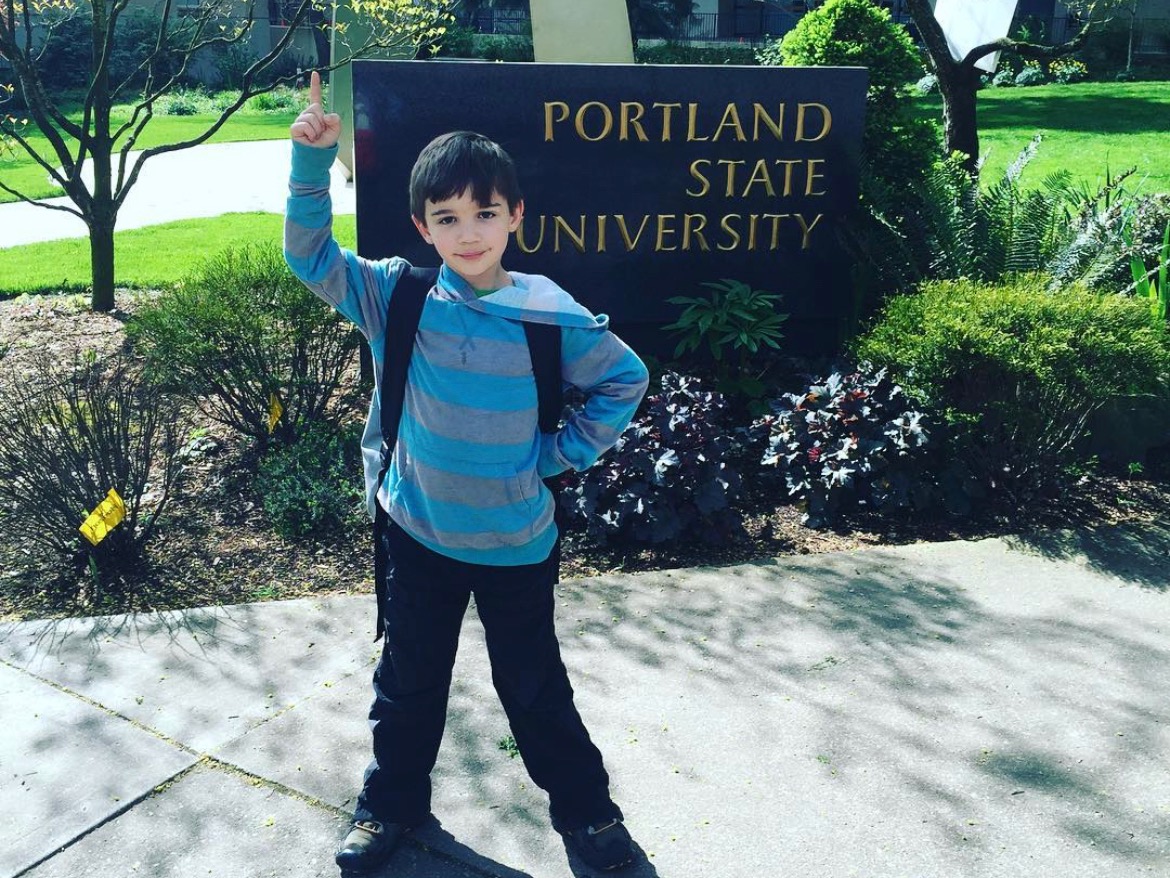 The image is of a child standing in front of a Portland State University sign. 