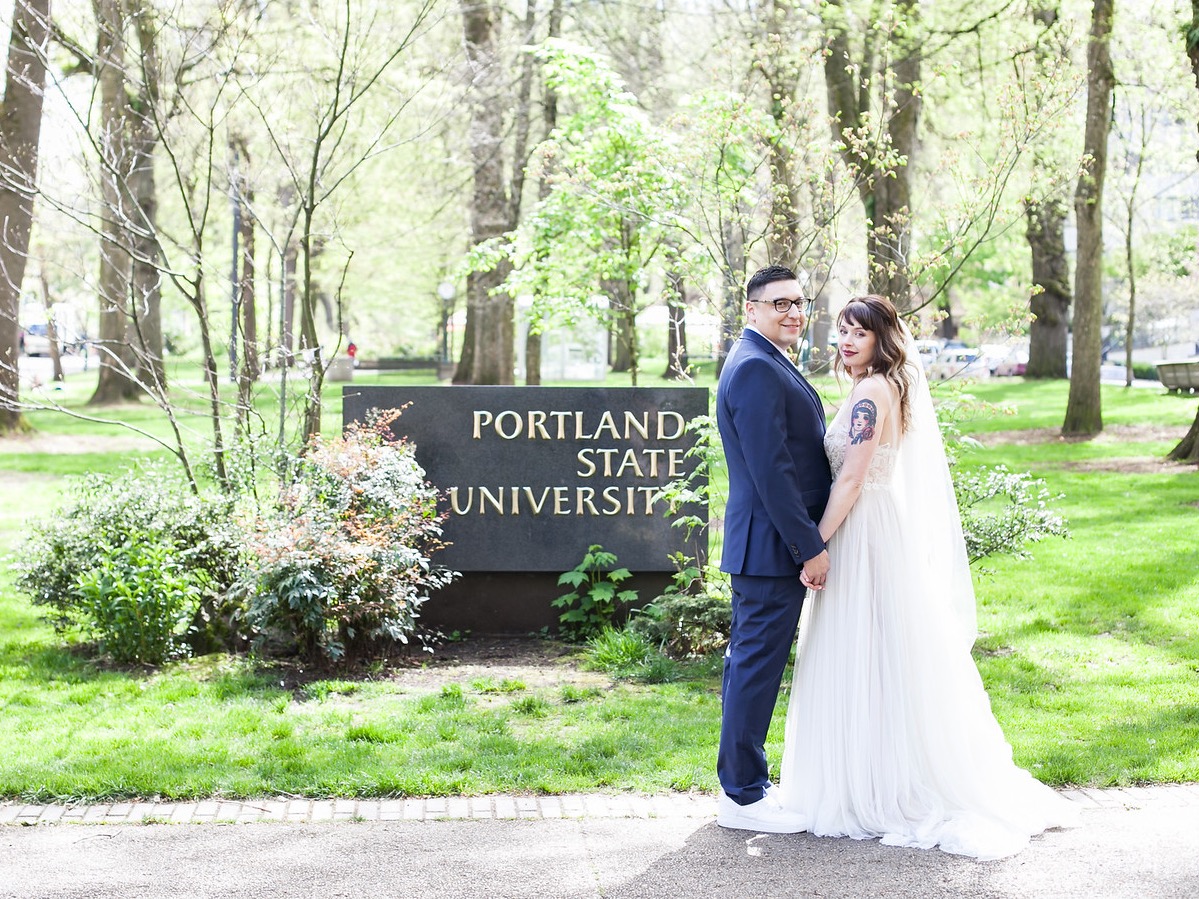 The image is of a couple wearing wedding clothes, standing in front of the Portland State University sign. 