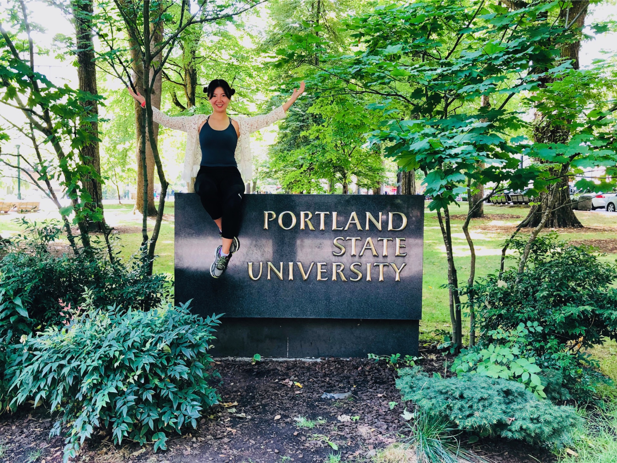 The image is of a person sitting on the Portland State University sign. 