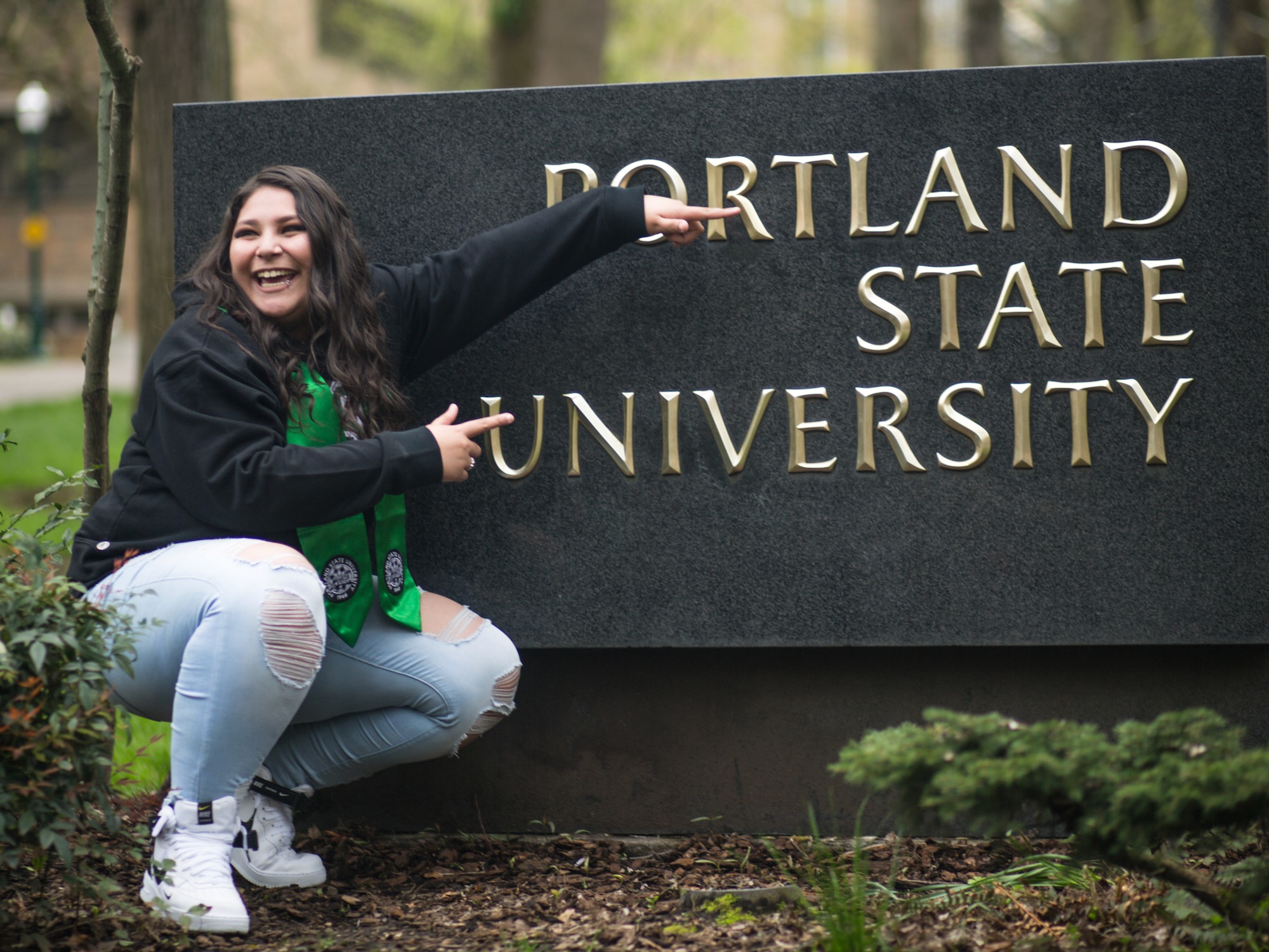 There is a person bent down pointing at the Portland State University sign.