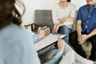 A therapist speaks with two individuals about their treatment schedule.