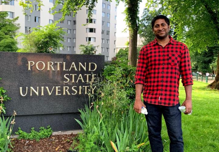 The image is a person standing in front of a Portland State University sign. 