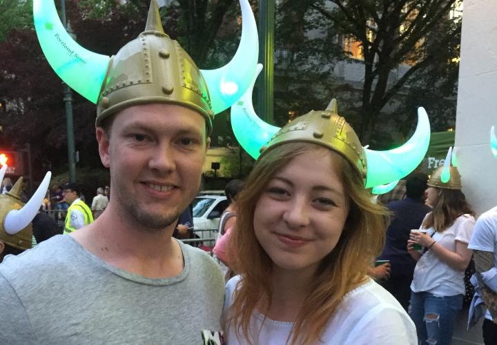 The image is of two people wearing viking hats while standing in a street, the horns on the hats are glowing green. 