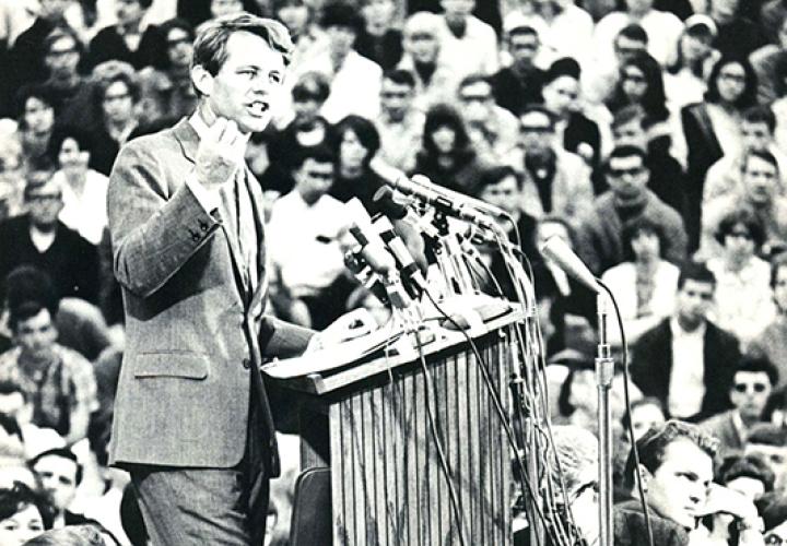 Robert F. Kennedy speaking at a podium in front of a large crowd. 