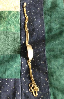 There is a gold bracelet on a green and black blanket.