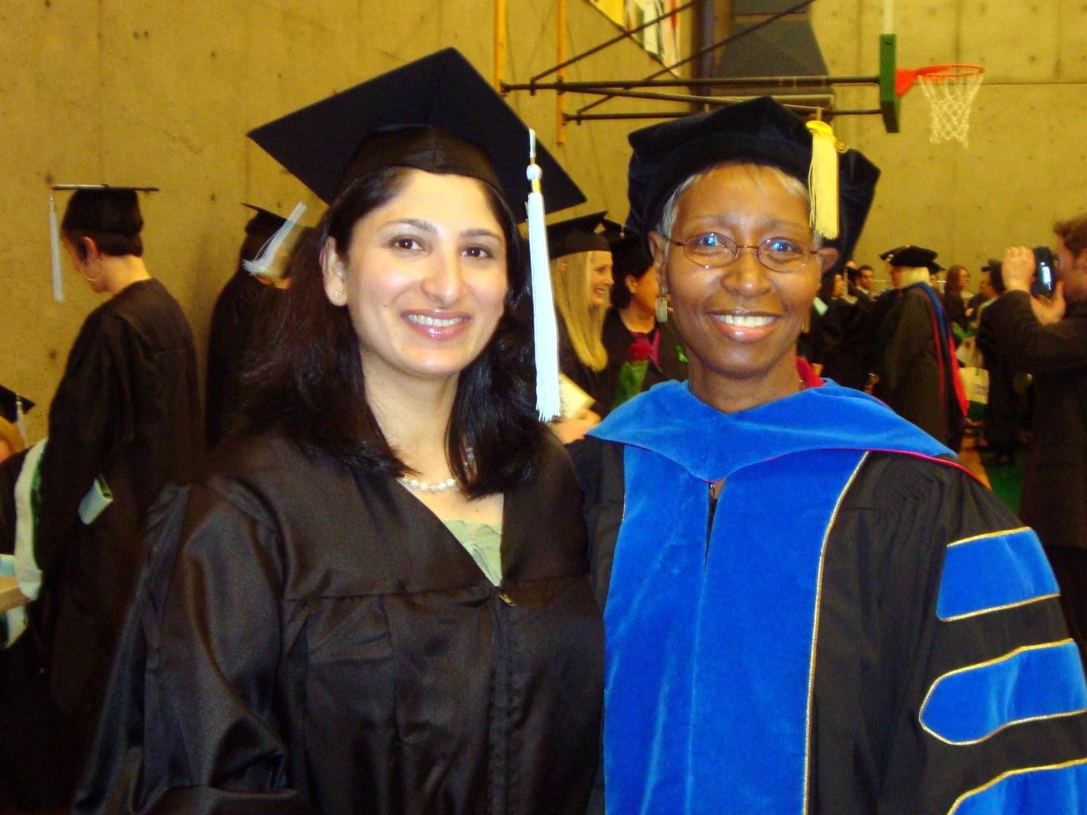 The image is of two people standing together and wearing graduation regalia, they are smiling for the camera. 