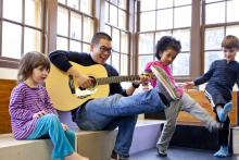 Person playing the guitar sitting with kids