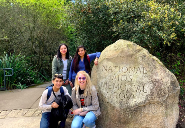 Students on an Alternative Spring Break trip pose next to a rock engraved with the words National Aids Memorial Grove