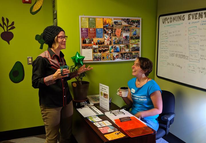 Two individuals talk across the front desk fo the Hub for Service & Sustainability while holding mugs of tea