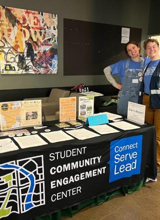 2 Students standing by the student community engagement center table