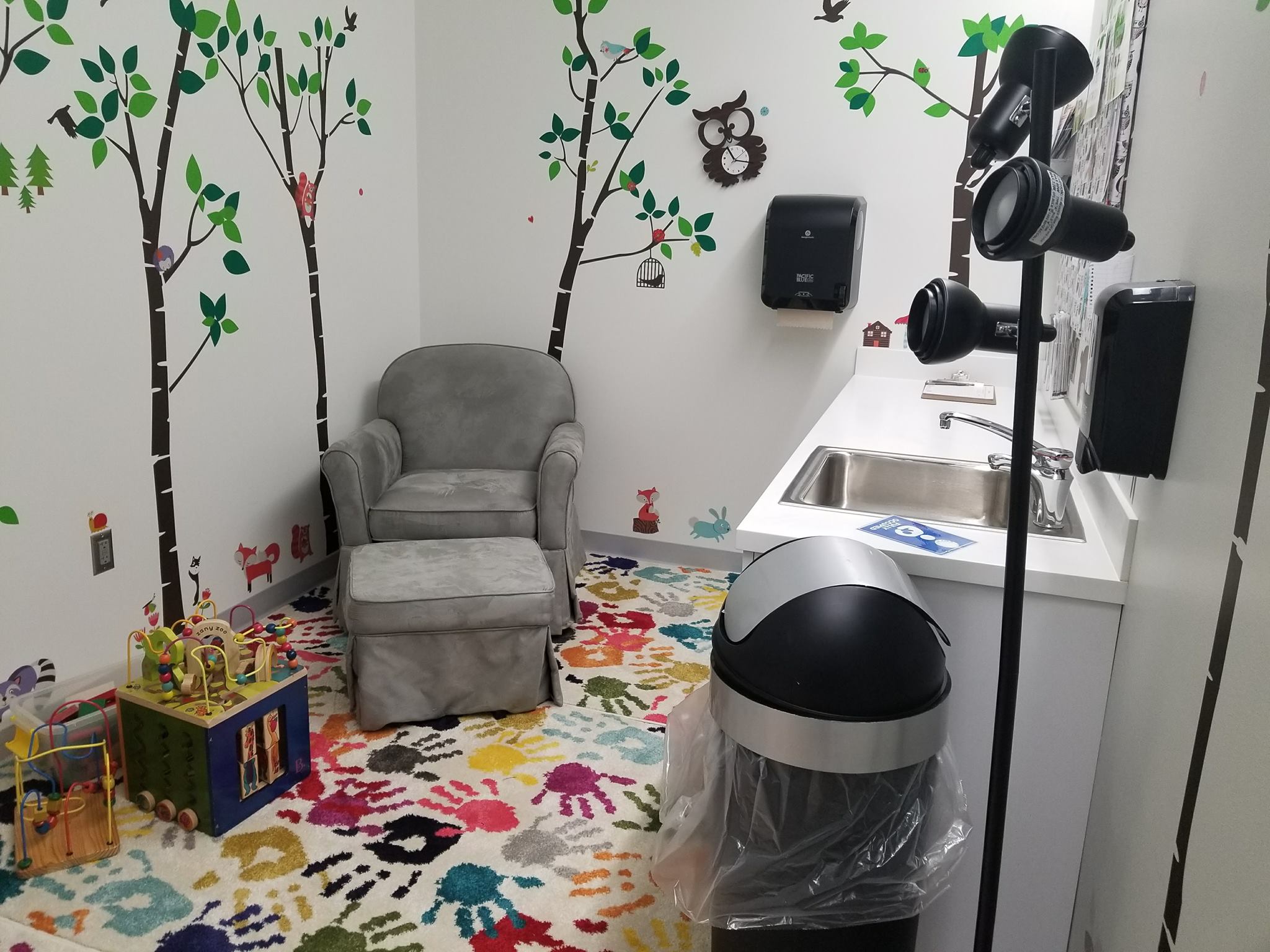 Lactation room equipped with a chair, foot rest, sink, trashcan, and children's toys.