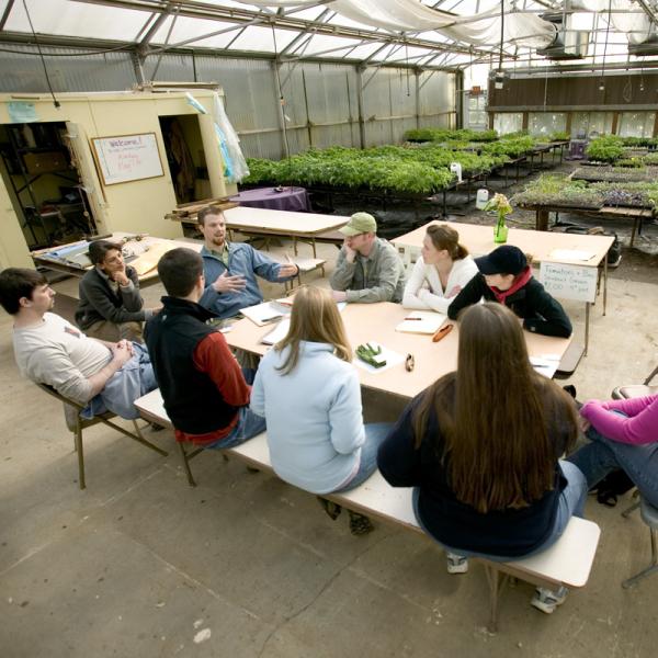 several people sitting around a table with greenhouse plants behind them