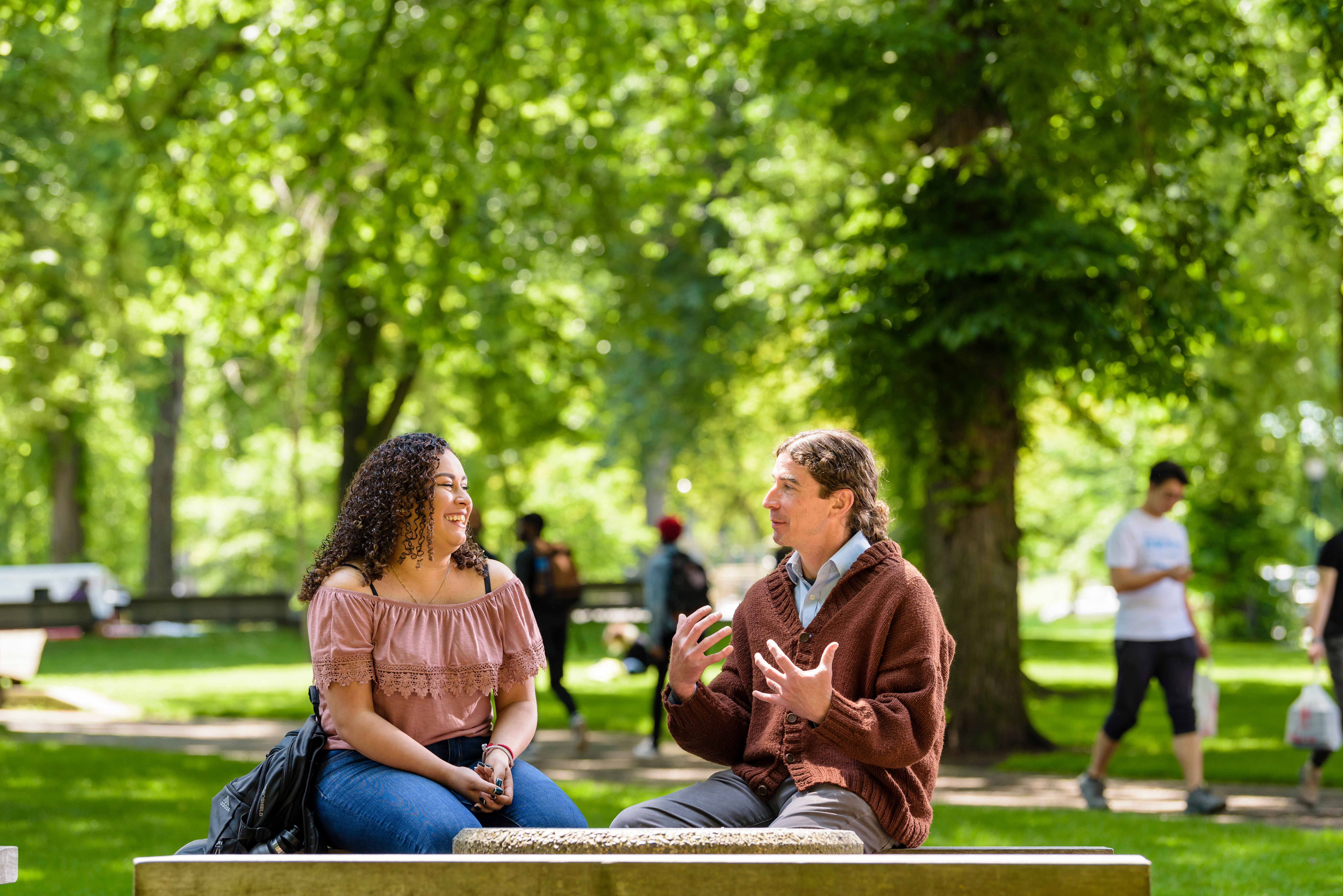 two individuals sitting on a bench in the PSU Park Blocks engaged in conversation