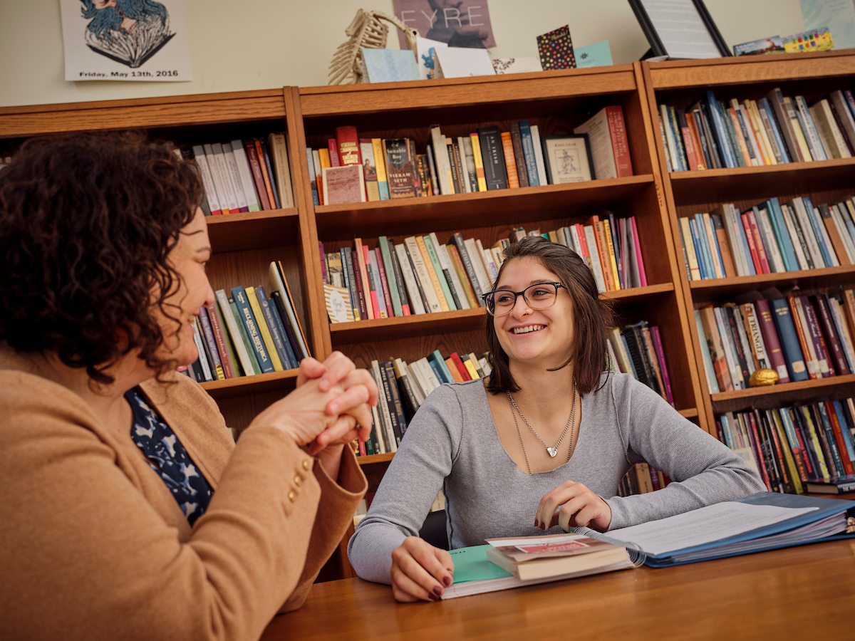 Image of two individuals in library sitting and smiling.