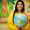 student holding a globe stands in front of a mural