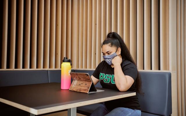 student with a face mask studying inside a PSU lounge