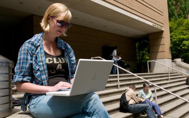 a student sitting on the steps of the library, working on a laptop