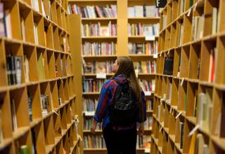 student wearing a backpack is walking through library bookshelves