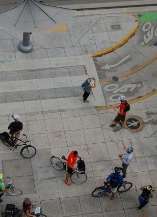 Aerial view of a sidewalk showing bike lane markings and pedestrian markings, with several cyclists and pedestrians moving through the space.
