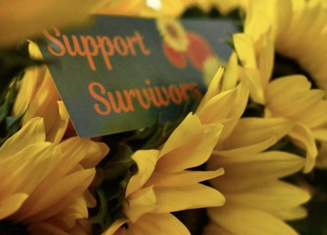 A teal bookmark with orange text reading "Support Survivors" rests in between a bouquet of yellow sunflowers