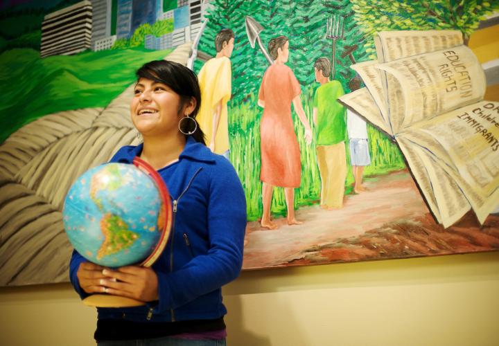 Student holding a globe in front of mural