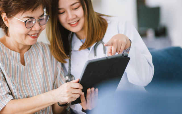 A young, female doctor is assisting an older, female patient access information on a tablet.