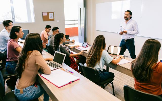 A group of students with computers in a classroom listening to an instructor