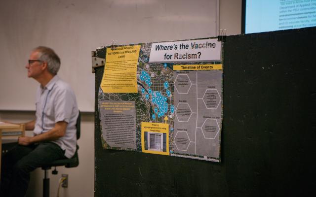 Professor next to poster, “Where’s the vaccine for racism?”