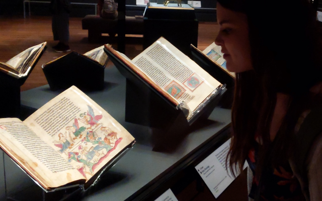 Woman at a museum looking at illuminated manuscripts on display.