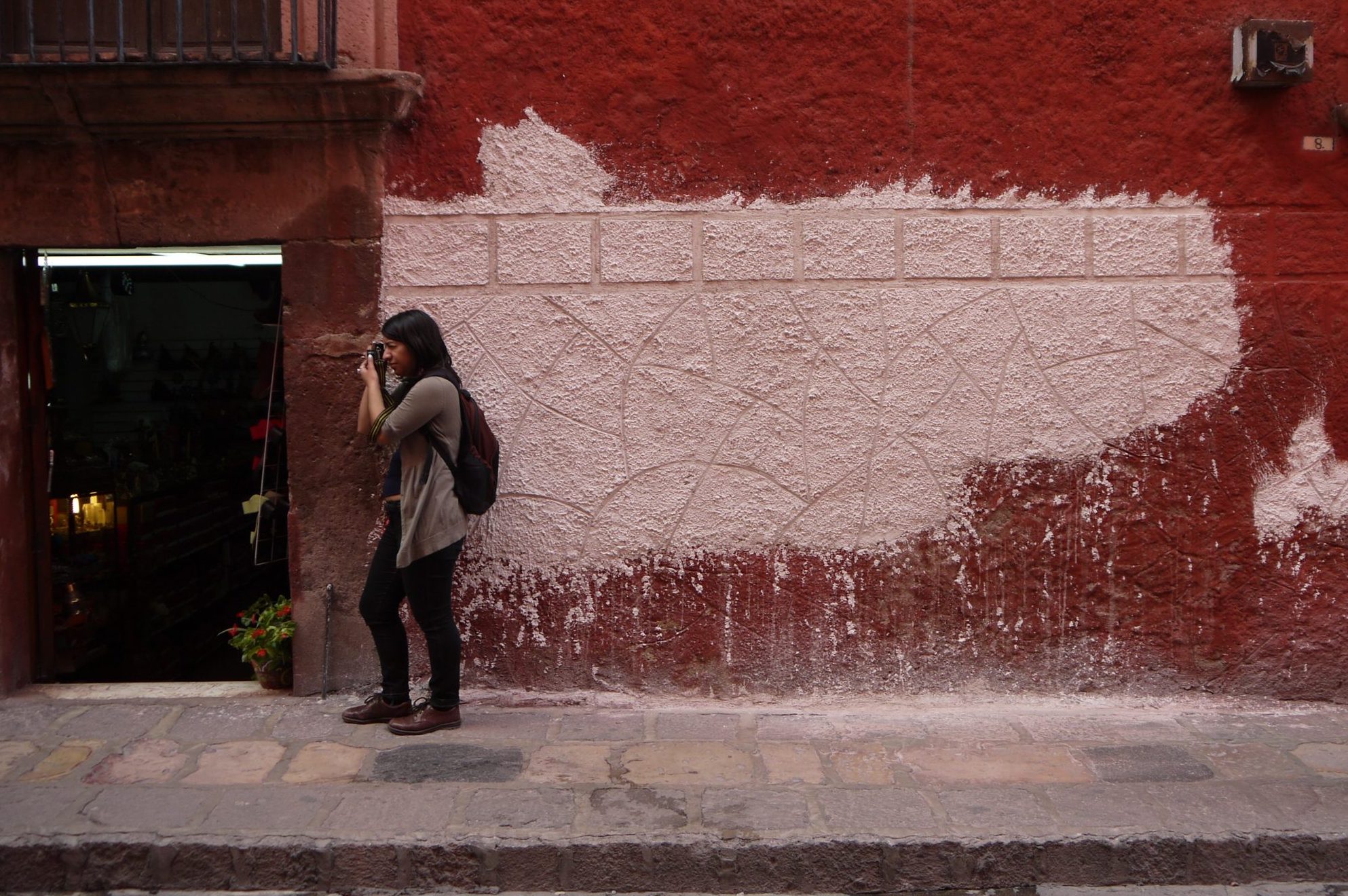 A woman in front of a colorful wall takes photos on a street in Guanajuato, Mexico