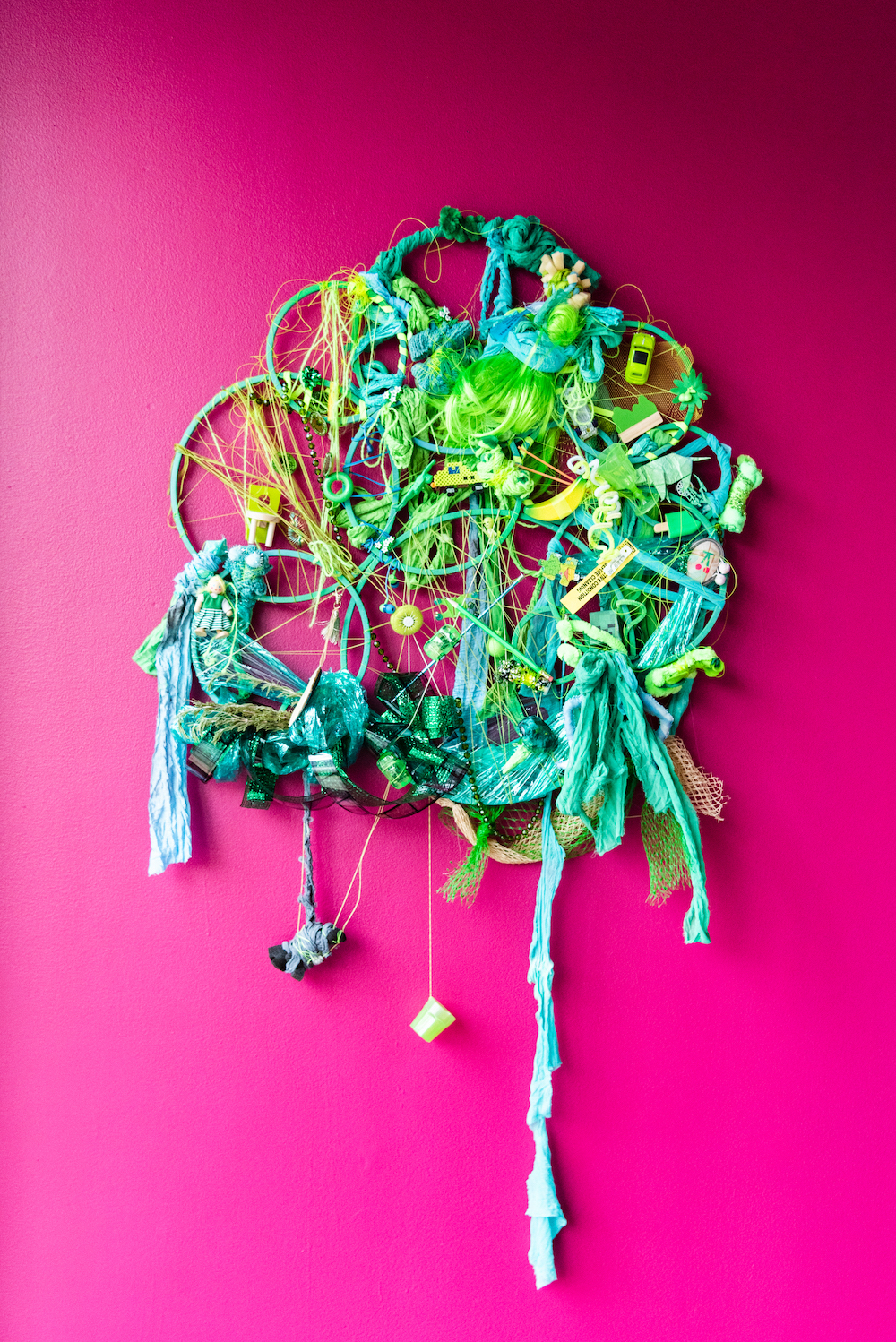 Mixed media assemblage in green tones on an vibrant pink wall