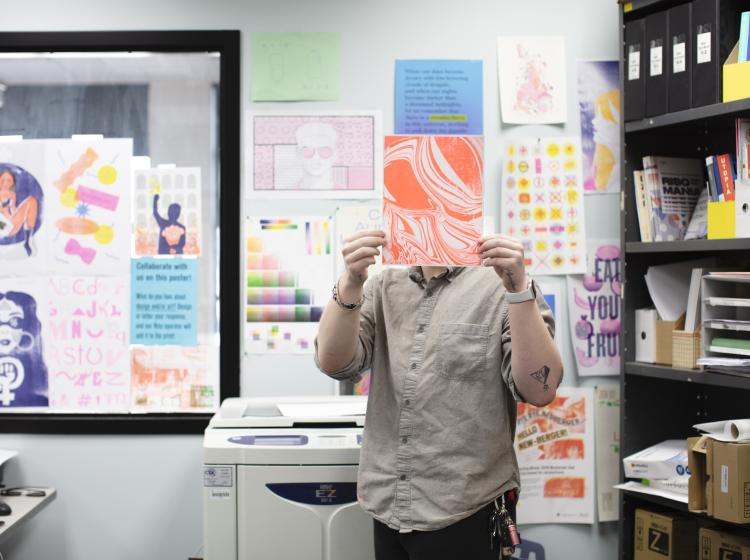 Student next to Risograph printer holding a Riso print